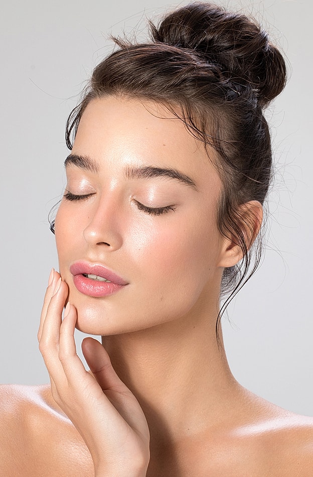 Woman with soft makeup and hand on face.